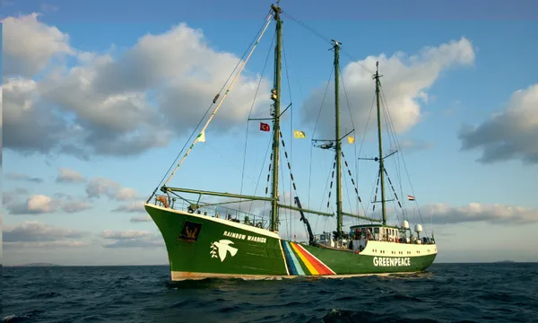 A photograph of the Greenpeace ship the Rainbow Warrior on the sea with a sunny blue sky with clumps of cloud above.