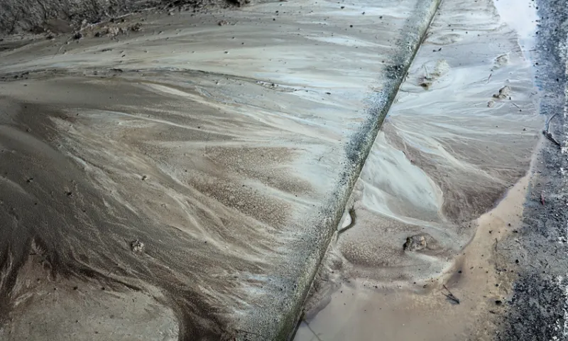 textured brown silt tipping into a drain