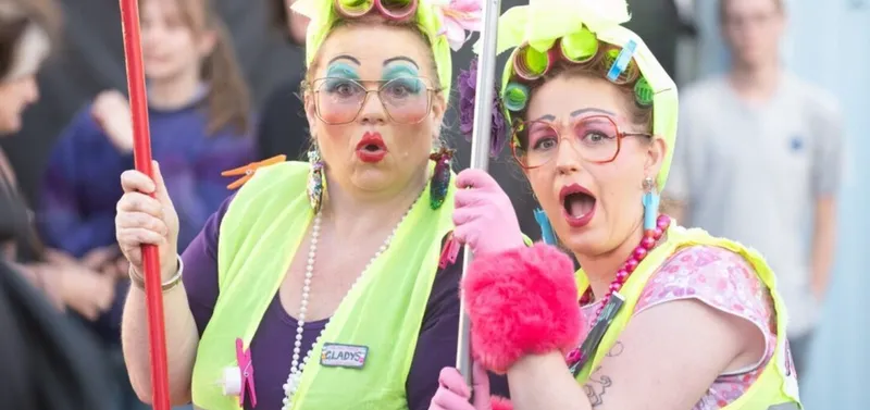 two ladies dress up wearing a lot of colourful make up hair rollers and high-vis vests