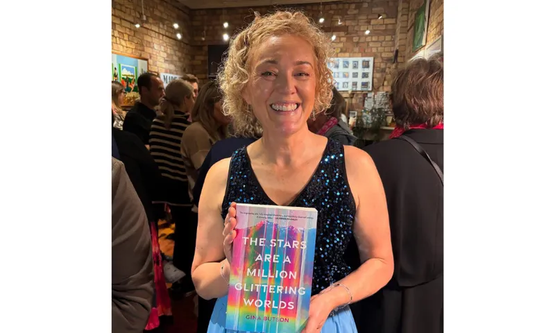 Photograph of a woman holding up her book in a crowded room and smiling.