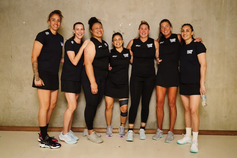 Seven netballers stand in a row and smile at the camera