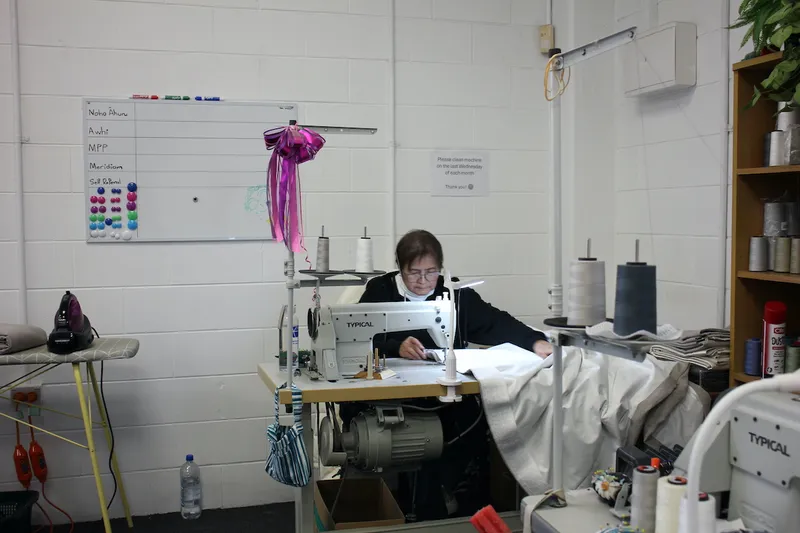woman sitting at an industrial sewing machine, guiding a curtain through.