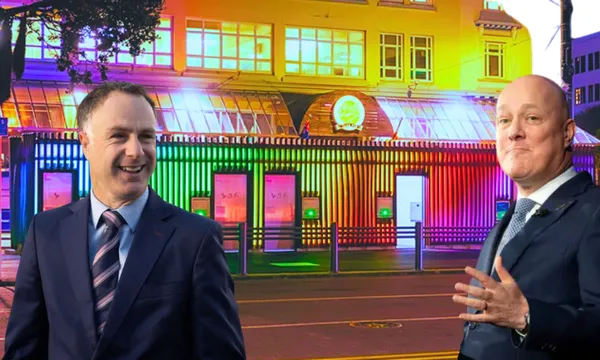 Two men in suits in front of a colourfully-lit building