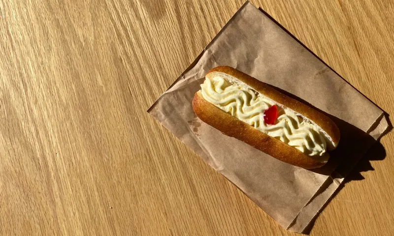 a cream donut with a red jam dot in the centre, on a wooden table
