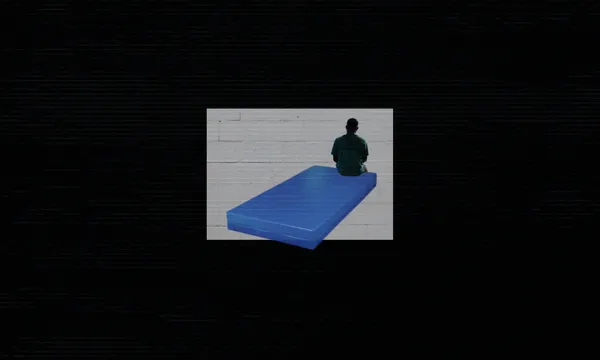 A black image with a small blue mattress in the centre and the silhouette of a person sitting on the edge of it