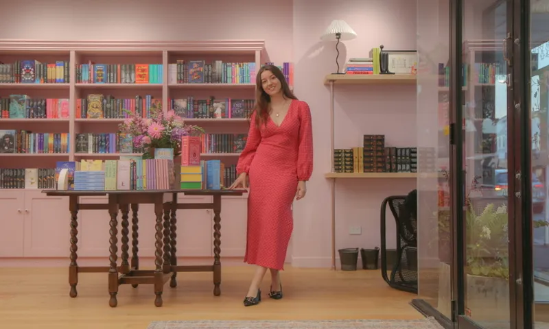 A woman in a red dress is standing in a bookshop. She is smiling.