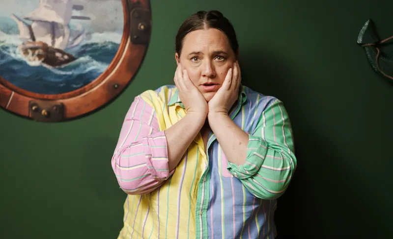 Alice Snedden wears a multicoloured pastel shirt and holds her face in her hands