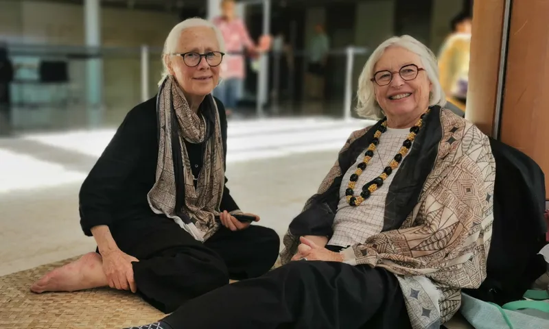 two women sitting on woven mats, smiling