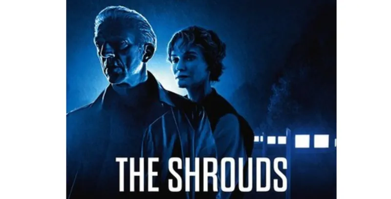 A film poster for The Shrouds which shows a man and a woman standing together looking into the distance. It is dark and there are a row of light behind them.