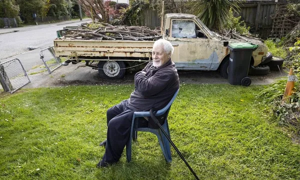a pakeha man with a rusty truck in the background sitting on a glowing green lawn