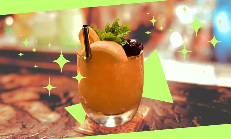 A cocktail garnished with a slice of grapefruit, mint leaves, and two cherries sits on a coaster, with a metal straw and sparkling graphic effects surrounding the drink.