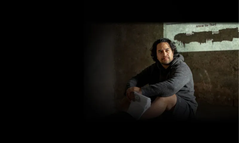 A young māori man is standing in front of the English version of the Treaty of Waitangi.