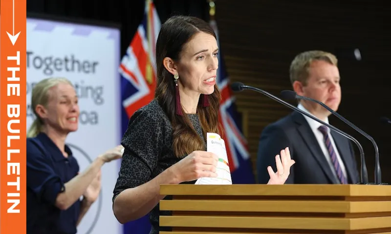 A woman speaks at a podium with New Zealand flags behind her, holding papers. A man stands beside her, and a sign language interpreter is visible in the background. A banner reads “Together fighting” with partial text visible.