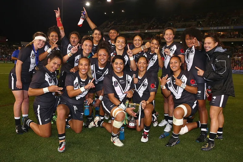 a team of women rugby league players in black uniforms celebrate to the camera