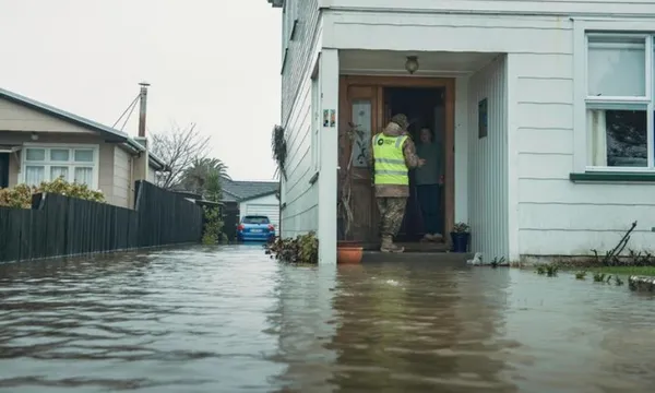 someone in high-vis gear knocks on a door of a house surrounded by water