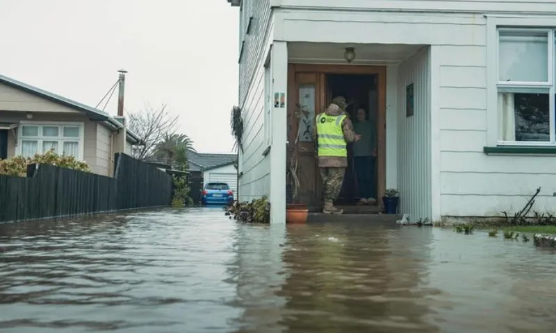 someone in high-vis gear knocks on a door of a house surrounded by water