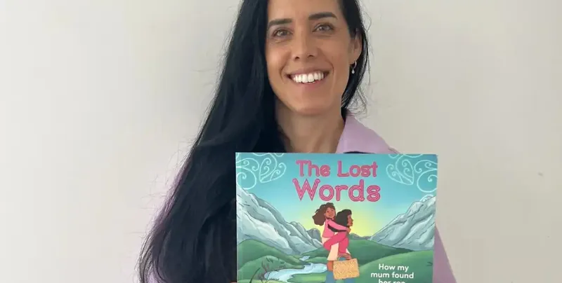A photo of a woman holding a picture book, she has long black hair and is smiling.