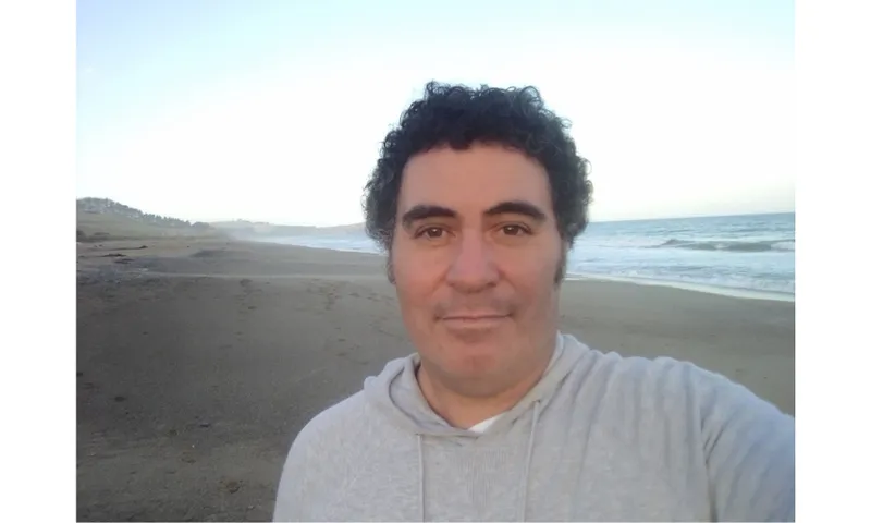 A photograph of a man standing on a beach.