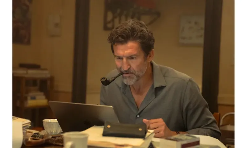 A still from a TV episode of a man with a pipe in his mouth leaning into a laptop.