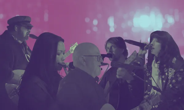 five musicians, including three men and two women, perform with guitars and microphones against a vibrant purple and blue background with blurred lights.