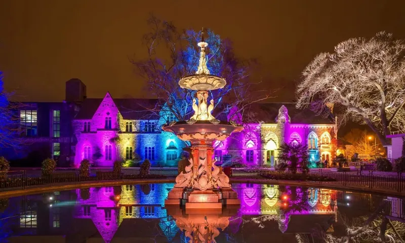 A photograph of a fountain lit up by multi coloured lights.