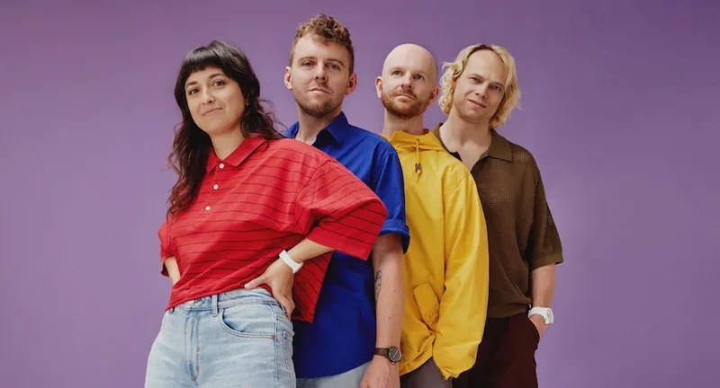 The Beths stand in primary coloured tshirts in front of a purple background