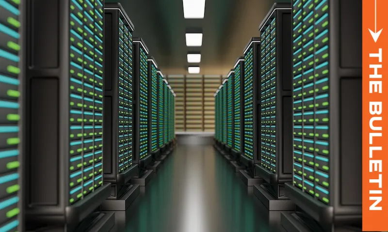 A row of server racks with glowing green and blue lights lines a hallway in a data center; "THE BULLETIN" is written vertically on an orange banner on the right side.