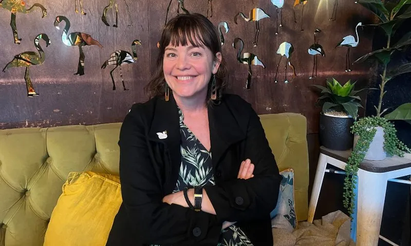 Julie Anne Genter, sitting on a green couch with her arms folding and grinning.