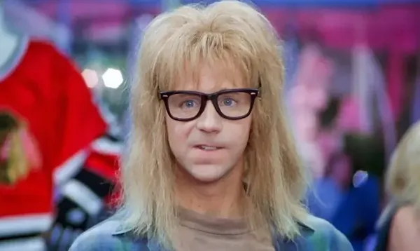 A man with a fluffy blonde mullet and glasses stares nervously at the camera