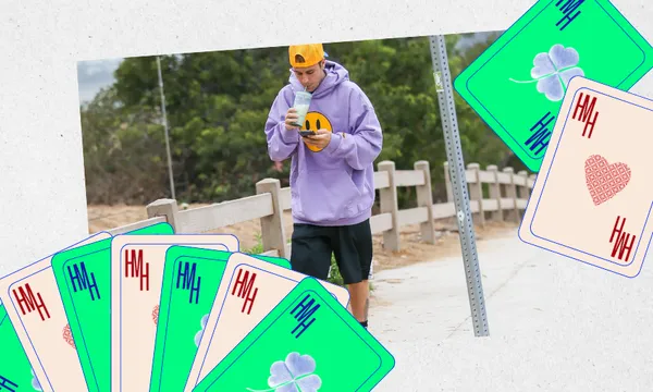 A person in a purple hoodie and yellow cap walks outside, looking at a phone. Large illustrated playing cards with hearts and clovers border the image in the foreground.