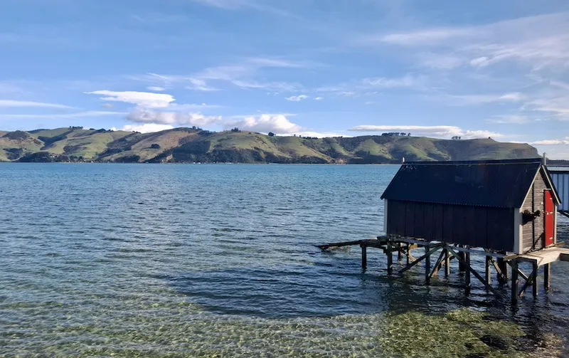 A picturesque scene at Otakou on the Otago Peninsula, with tranquil clear water and a boat shed