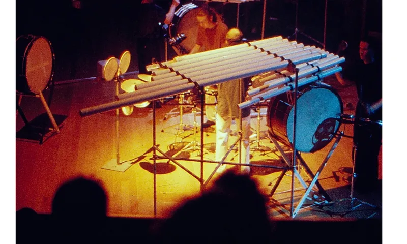 A blurry stage with large instruments set up. There are three musicians on stage and several percussion instruments.