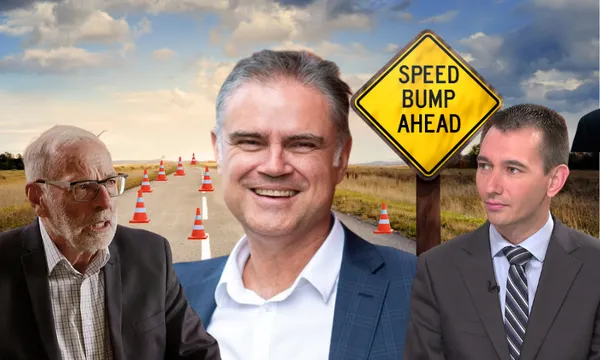 Three men in suits appear in the foreground of a rural road lined with traffic cones and a yellow "Speed Bump Ahead" sign under a cloudy sky. The man in the center is smiling, while the others appear serious.