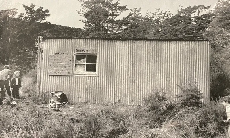 an old photo of a corrugated iron hut with a small window and trees surrounding it