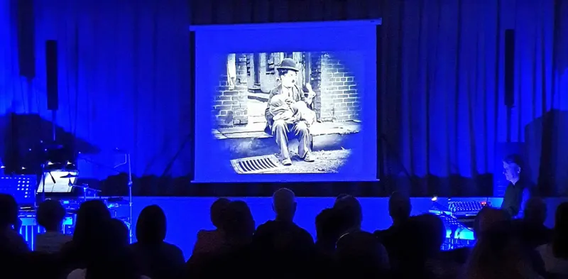 An image of a cinema screen showing a still of Charlie Chaplin. The audience is in silhouette and the tint is royal blue.