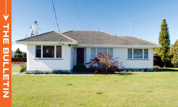 a single storey white house with a large flat front lawn and blue sky above