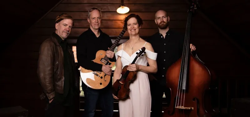 A photograph of a group of musicians. There is a double base, violin and guitar. They're all looking at the camera.