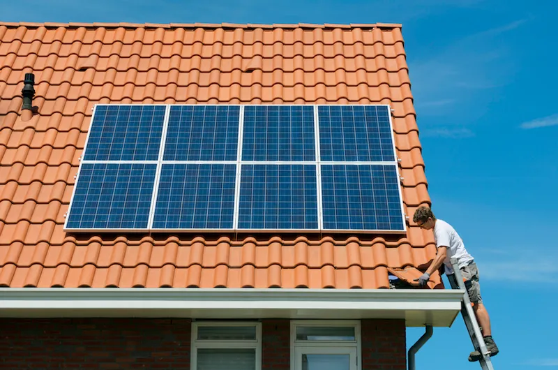 Worker checking installation of solar panels on roof of new home, Netherlands