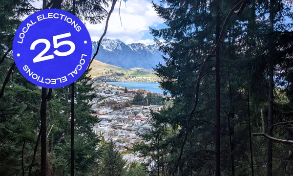 pine trees framing houses in central queenstown and the shining blue lake