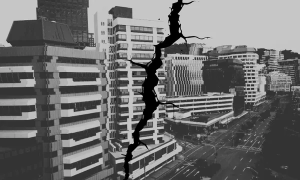 A black-and-white image of a cityscape with tall buildings and empty streets, featuring a large jagged crack digitally superimposed vertically through the center of the scene.