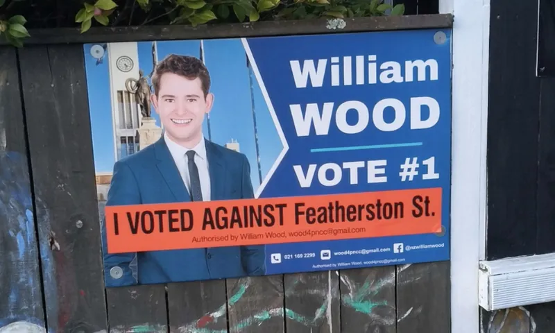 a blue nationalish sign with a young man in a suit and the words 'I voted AGAINST featherston St"