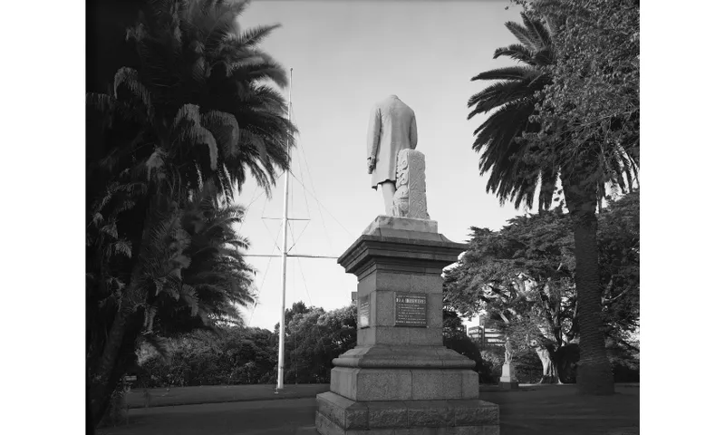 A black and white photo of an outdoor monument - the figure of a man - showing the figure's head has been chopped off.