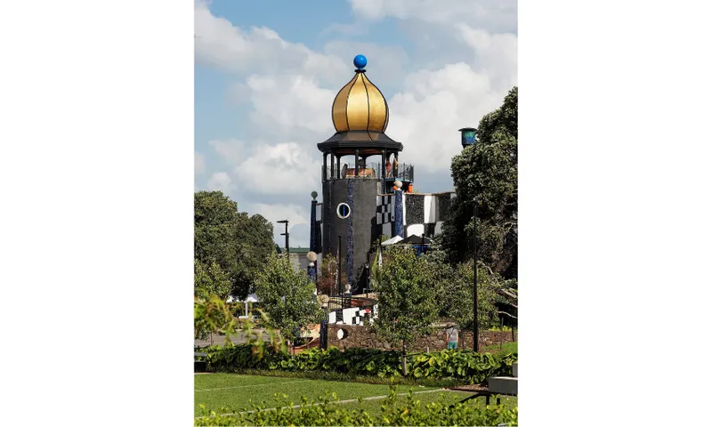 Photograph of the Hundertwasser Centre in Whangārei showing a garden and lawn with a golden tower in the background.