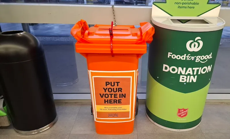 A photo of a rubbish bin, an orange ballot bin, and a food donation bin