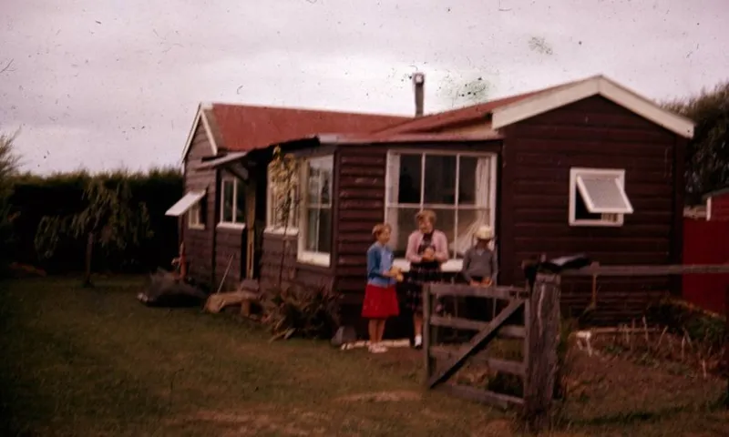 An old photograph of a woman and three children standing outside a wooden hut in Milford.