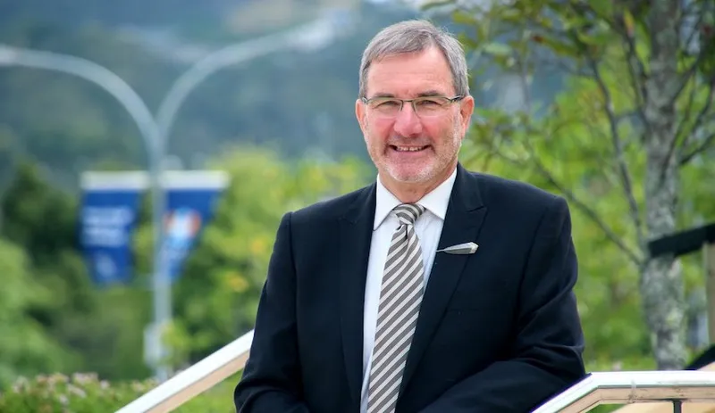 Paul Spoonley wears a suit and tie and smiles in front of some trees