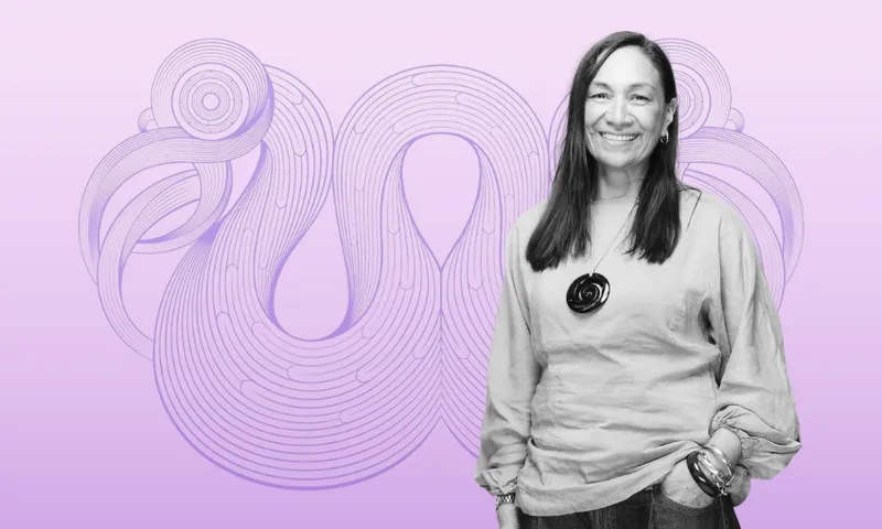 A smiling woman with long hair stands in front of a purple abstract swirl design on a gradient lavender background. She wears a light blouse, pants, and a round pendant necklace.