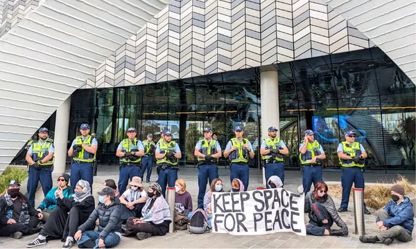 people sit on the ground under an arch with hi vis wearing police officers behind them