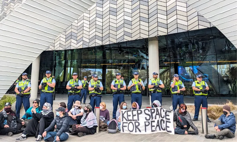 people sit on the ground under an arch with hi vis wearing police officers behind them