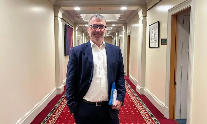Duncan Webb stands and smiles in the middle of a hallway in parliament.